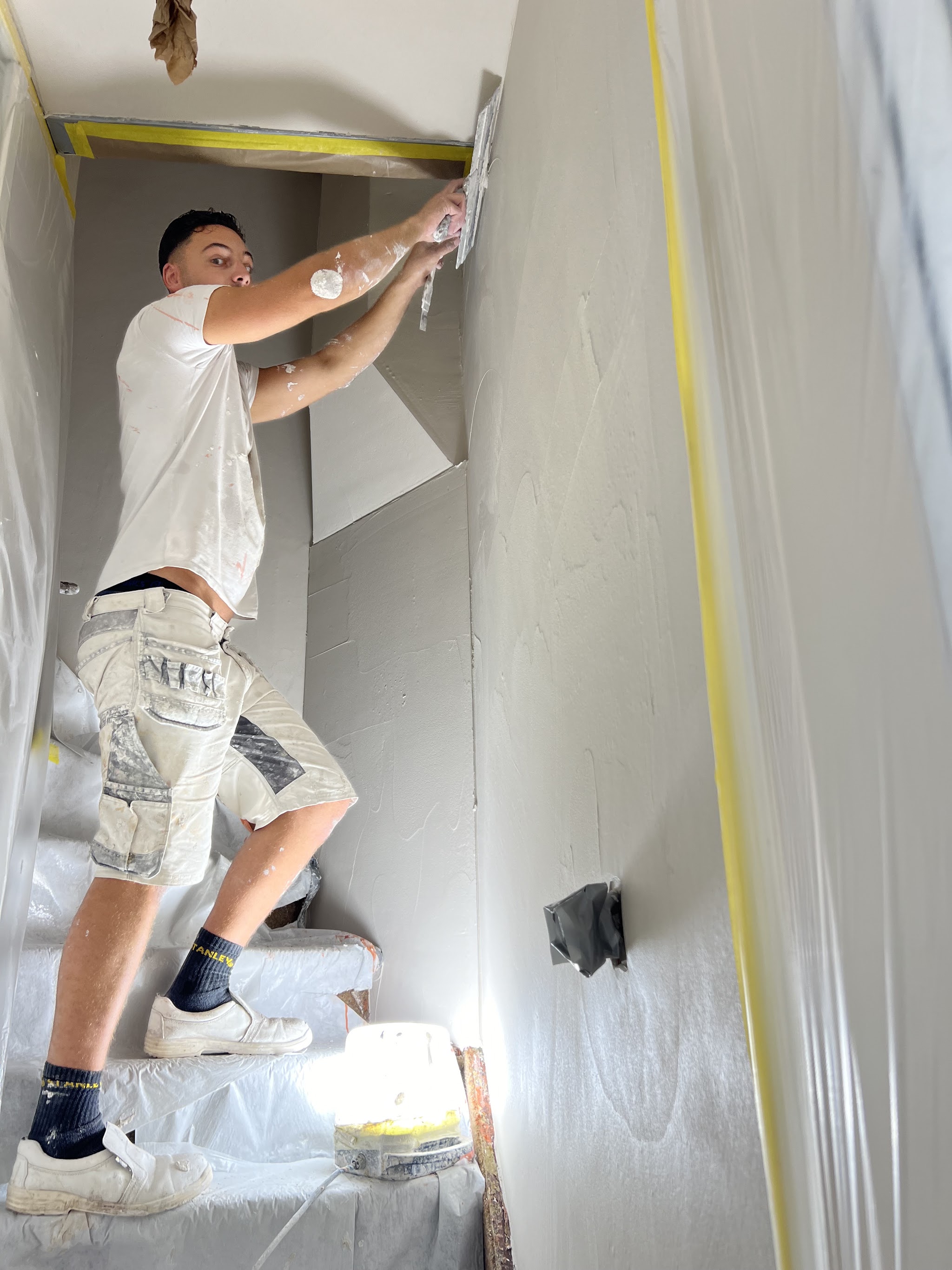 Darrell aan het werk met de spaan op een wand in de traphal, de trap is afgedekt